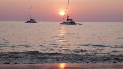 Sailboats in front of pastel colored sunset at beach - ultra slow motion tilting up