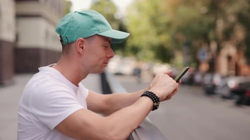 Man in Cap Using Smartphone at Summer City