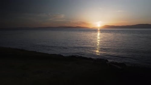 Cinematic view of sun setting down behind mountain range and seawater, static view