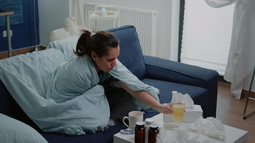 Woman Wrapped in Blanket Drinks Beverage on Couch
