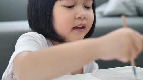 Close up happy Asian girl drawing picture with water color on paper.