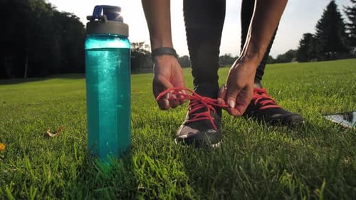 Woman Tying Shoes With Water Bottle on Lawn
