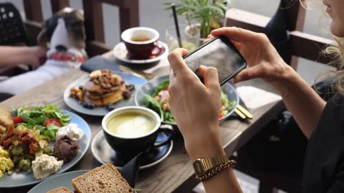 Girl Taking Pictures of Healthy Vegan Brunch in City Cafe with Smartphone. Food Blogging Concept