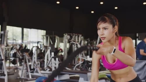 Sporty asian woman working out with battle ropes at gym.