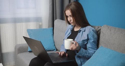Jolie jeune femme se relaxant à la maison avec un ordinateur portable et un café