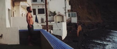 Homem de pé na varanda olhando para o pôr do sol à beira-mar