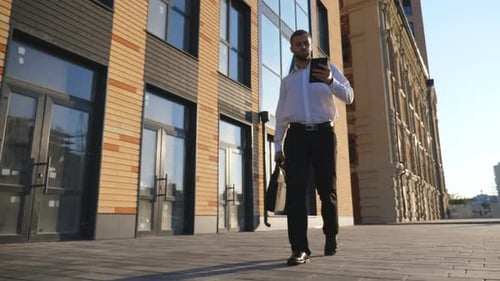 Successful Entrepreneur in Formal Wear Uses Smartphone Walking Near Office Building