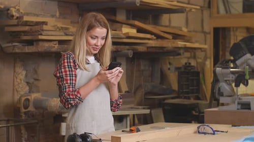Woman Uses Cell Phone in Woodworking Workshop