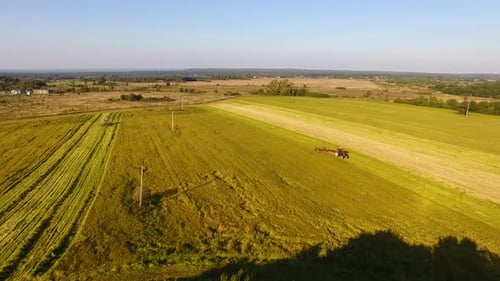 The tractor is stacking haystacks on an agricultural field in autumn, aerial view