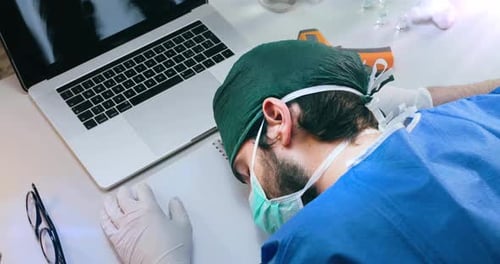 Tired Doctor Resting Head Next To Laptop