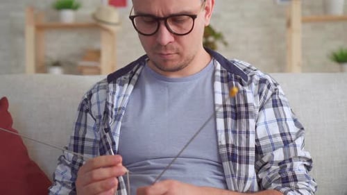Man Knitting on Sofa with Needles and Yarn