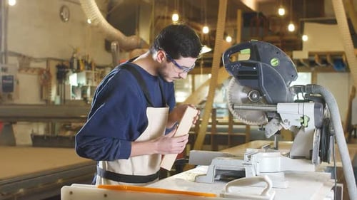 Focused Man Cutting Wood with Miter Saw in Workshop