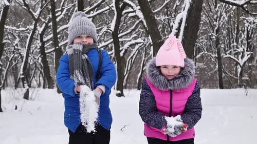Kinder, ein Junge und ein Mädchen im Wald im Winter, springen, werfen Schnee und lachen