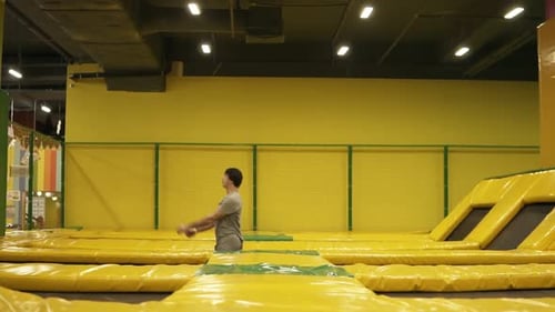 Young Male Athlete in Beige Tshirt and Shorts Hopping on Trampoline with Somersault and Body Twist