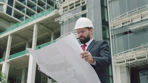 Engineer Male in a White Safety Helmet Developer at a Construction Site Checks on the Drawings at