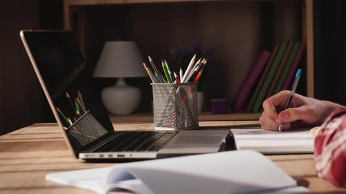 Student Writes in Notebook Works at Home Near Laptop