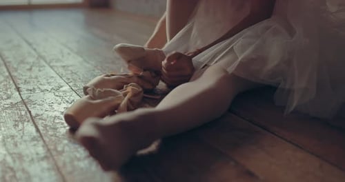 Ballerina Putting on Ballet Shoes on Wooden Floor