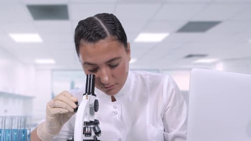 A Female Medical Professional Looks at Biological Samples Under a Microscope and Writes Data
