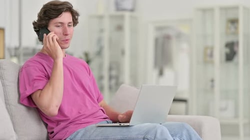 Man on Sofa Talking on Phone With Laptop