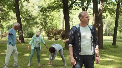 Fit Man Observes Seniors Stretching in Green Park
