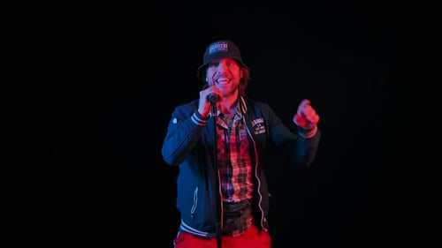 Charismatic Musician Sings Into a Microphone in a Dark Studio on a Black Background in the Light of