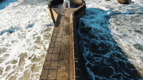 Ocean Beats Lighthouse Base Making Foam Against Horizon