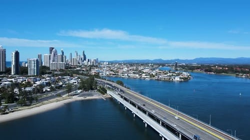 Ein stark frequentiertes städtisches Straßennetz und eine Brücke, die sich über ein großes Gewässer erstrecken und zu einer Metropole führen