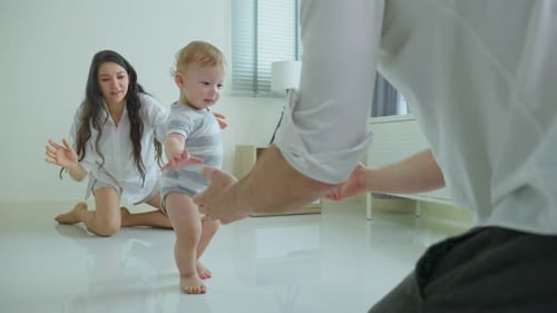Caucasian cute baby boy child learn to walk on floor with parent's support in living room at home.