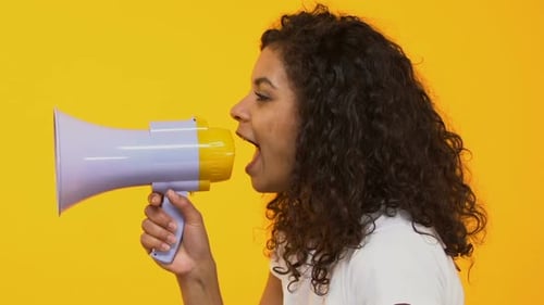 Young Woman Speaking into a Megaphone on Yellow Background