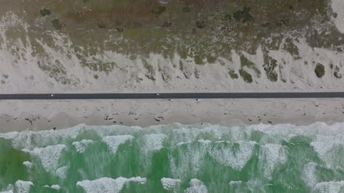Top Down Horizontally Panning Footage of Straight Coastal Road Passing Along Waves Washing Sand