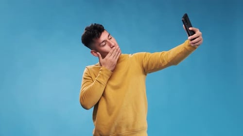 Young Adult Poses for Smartphone Selfie on Blue
