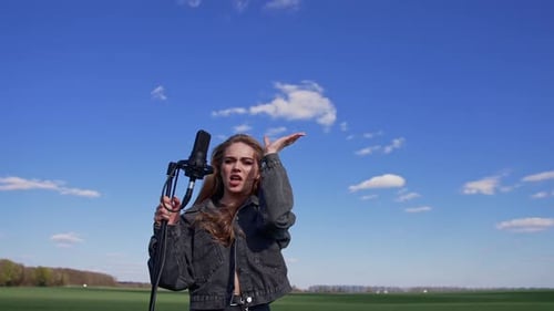Woman Singing into Microphone Outdoors on Green Field