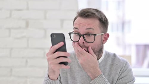 Man Looks at Mobile Phone with Shocked Expression
