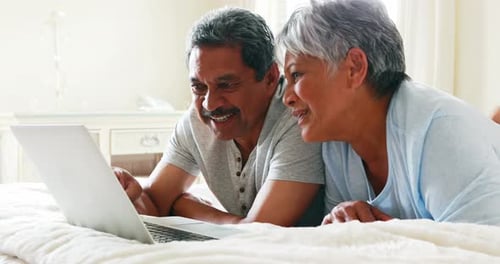Senior Couple Relaxing With Laptop Computer on Bed