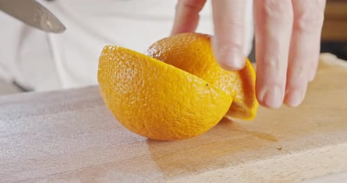 Close up of a chef knife peeling and slicing an orange