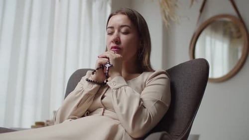 Woman Holding Rosary Praying Peacefully in Home