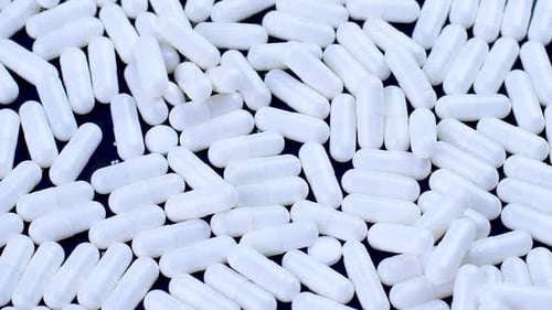 White Antiviral Capsules Lie and Rotate on a Black Background