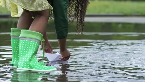 Child Playing with Paper Boat in Large Puddle