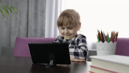 Girl Smiles and Waves at Tablet at Desk