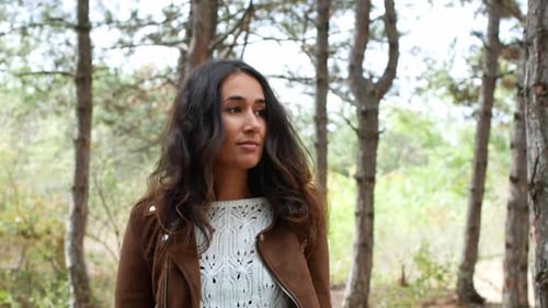 A beautiful young woman in a stylish hat is walking through the woods.