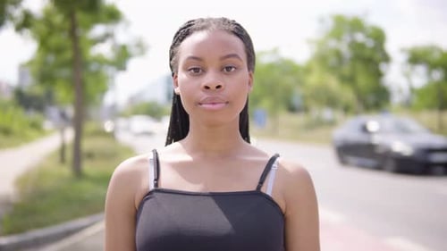 Une jeune femme noire enlève son masque facial et regarde la caméra - une route très fréquentée dans une zone urbaine