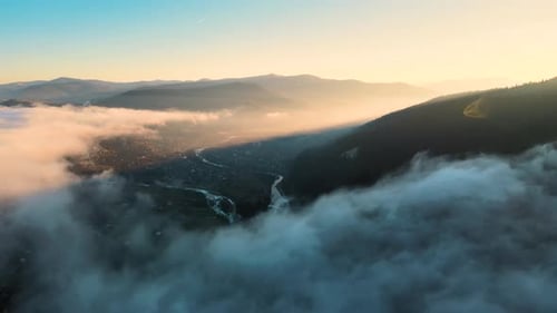 View from above of vibrant landscape of foggy clouds covering mountain hills and village