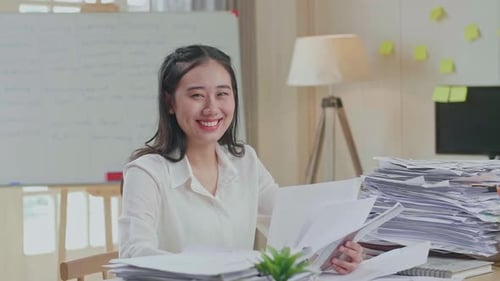 Asian Woman Smiling To Camera While Working With Documents At The Office