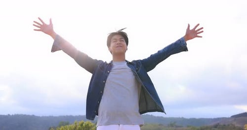 Freedom Asian young man raising hands on the top at the mountain.