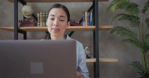 Close Up Portrait of Smiling Asian Teacher Conducts an Online Lesson Using Laptop