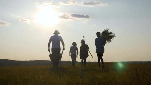 Young Family Having Fun Outdoors in Their Farm. Gardener Dad Pushing Wheelbarrow with Vegetables at