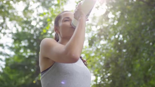 Attractive Sportswoman Drinking Water after Exercising in Park