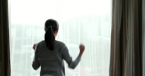 Woman Stretches and Opens Curtains to City View