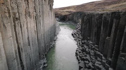 Aerial dolly past basalt columns of Studlagil Canyon, Iceland, above river.