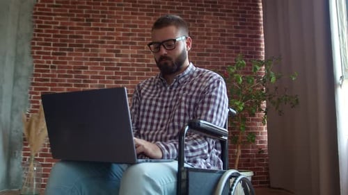 Man in Wheelchair Working with Laptop at Home
